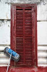 Old fashioned mop leaning against some closed rustic wooden shutters in a basic white stone dwelling