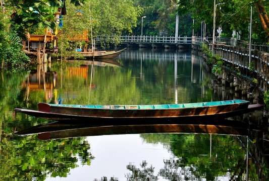 Old rustic wooden boat on a calm backwater canal in Asia. the was is calm and shows a perfect mirror image reflection. 