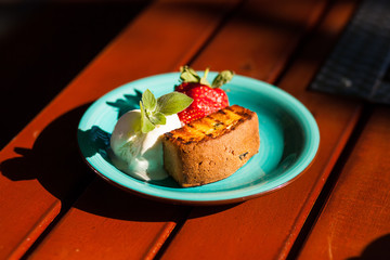 Strawberries with ice cream and biscuits on a blue plate standing on a wooden table
