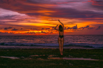 Beautiful young girl model with perfect body and sexy booty in black bikini poses on the ocean beach at awesome colorful sunset background on Bali. Outdoor summer travel photo with female model