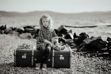 Sad child sitting on a suitcase and playing with his toy