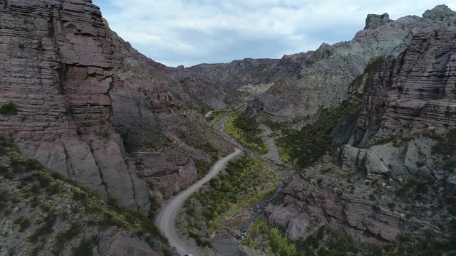 Aerial drone scene of Atuel river canyon in San Rafael, Mendoza, Cuyo Argentina. Camera moving forwards tracking modern new 4x4 van. Gravel street next trees and river. Colorfull rocks.