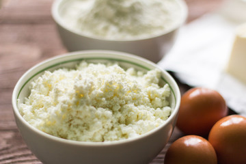 fresh rustic cottage cheese and eggs on wooden background, baking ingredients