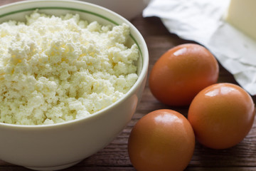 fresh rustic cottage cheese and eggs on wooden background, baking ingredients