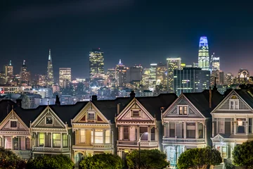 Foto op Plexiglas Backed by the night skyline of the city of San Francisco, California, the Victorian era houses near Alamo Square Park, are painted in colors to accentuate their architectural details. © Kenneth Keifer