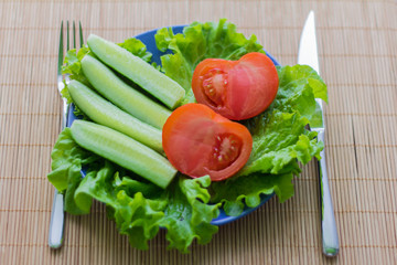 sliced cucumber and tomato with salad in plate on wooden background