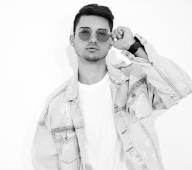 Portrait of handsome young model man dressed in jeans clothes in sunglasses posing on white background. Isolated