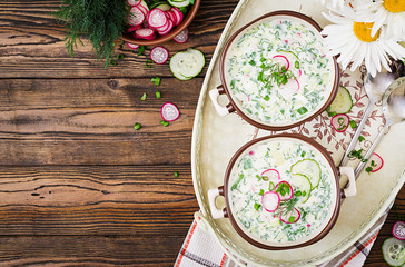 Cold soup with fresh cucumbers, radishes with yoghurt in bowl on wooden background. Traditional russian food - okroshka. Vegetarian meal. Top view. Flat lay