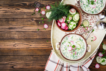 Fototapeta na wymiar Cold soup with fresh cucumbers, radishes with yoghurt in bowl on wooden background. Traditional russian food - okroshka. Vegetarian meal. Top view. Flat lay