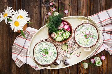 Cold soup with fresh cucumbers, radishes with yoghurt in bowl on wooden background. Traditional russian food - okroshka. Vegetarian meal. Top view. Flat lay