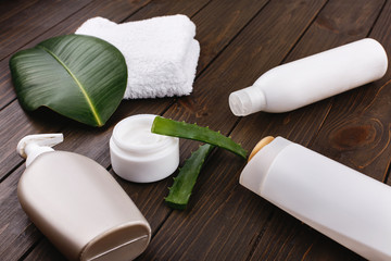 White towel, bottles of shampoo and conditioner lie on a table with green leaf and aloe