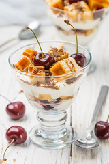 Dessert of waffles, cream cheese (ricotta, mascarpone, yogurt) and fresh cherries with chocolate chips in a glass. Delicious gourmet Breakfast