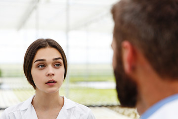 Man and woman in laboratory robes talk to each other standing in the greenhouse