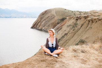 Naklejka na ściany i meble The girl is meditating on the edge of the cliff above the sea.