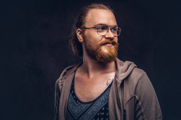 Fototapeta premium Close-up portrait of a redhead hipster male dressed in casual clothes standing in a studio, looking away. Isolated on a dark background.