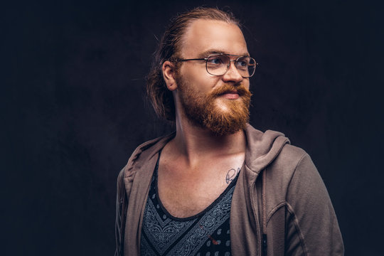 Close-up portrait of a redhead hipster male dressed in casual clothes standing in a studio, looking away. Isolated on a dark background.