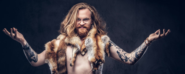 Naked tattoed redhead hipster male with long luxuriant hair and full beard posing with the fox...