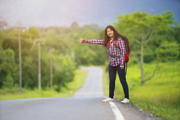 backpacker woman hitchhiking on the road with nature background