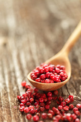 Red peppercorns  in a spoon on wooden table.