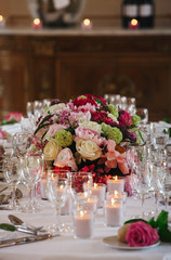 Wedding dinner table decorated with shiny pink candles and red flowers