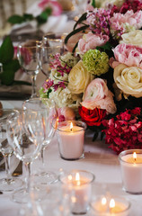 Wedding dinner table decorated with shiny pink candles and red flowers