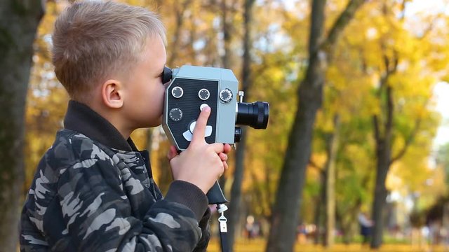 Child playing vintage old movie camera outdoors in golden autumn park. Kid happy to try making own video film with retro camera. Real time full hd video footage.