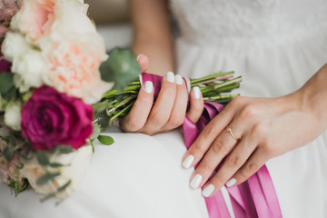 Beautiful colorful wedding flowers in hands of young bride sitting alone in home interior....