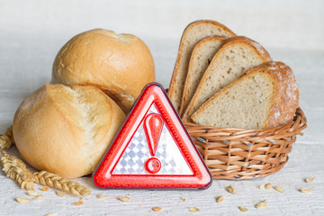 Gluten intolerance with bread wheat and warning sign on white planks
