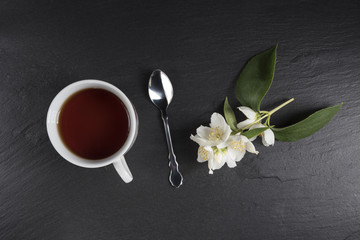Obraz na płótnie Canvas A cup of tea with jasmine flowers on a dark background. Top view.