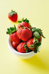 Fresh ripe strawberries on a white bowl on a yellow background. Copy space. Overhead view.
