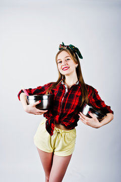 Young funny housewife in checkered shirt and yellow shorts pin up style with two saucepan isolated on white background.