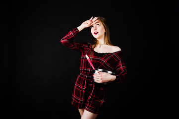 Young housewife in checkered dress with saucepan and kitchen spoon isolated on black background.