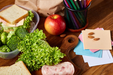 Tasty lunch with green lettuce and vegetables in container and school supplies, on wooden desk, selective focus.