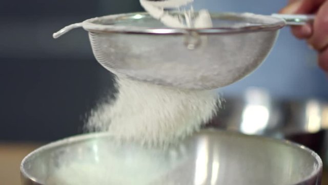 Close up shot of unrecognizable cook holding sieve and sifting flour into metal container when baking food
