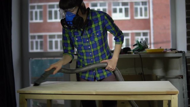 The process of building a wooden table, a woman carpenter removes the wood dust from the countertop using a vacuum cleaner in the workshop, slow motion. Preparation of the product for coating.