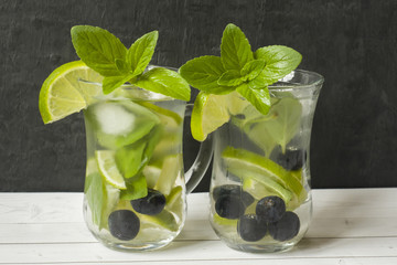 Summer refreshing drinks lemonade or cocktail Mojito with lime fresh mint blueberry ice. Light table, Dark wall