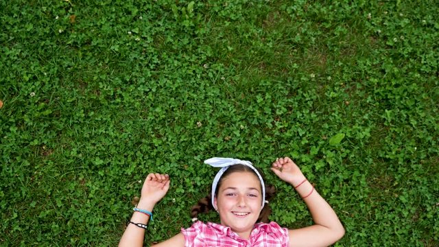 Caucasian young girl lying down on the grass in the park. Slow motion footage