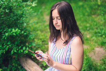 Girl sitting on bench with phone on background of forest