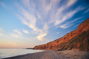 Sunrise / sunset on the mountainous ocean coast, with blue sky and feather clouds.