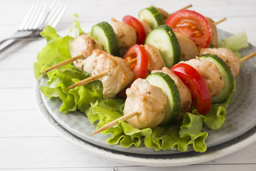 Traditional chicken kebab on wooden skewers with tomatoes, cucumbers and fresh herbs on a plate.