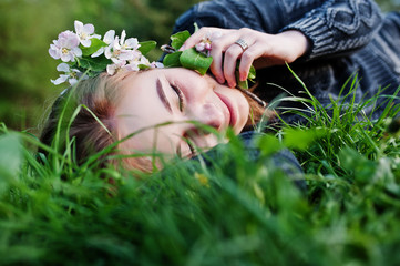 Young brunette girl lying on green grass with branches of blossom tree.