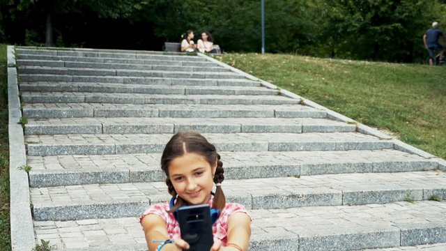 Pretty girl sitting on her skateboard on the stairs in park and looking at the smartphone. Slow motion footage