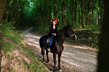 Mystical girl in wreath wear in black at horse in wood.