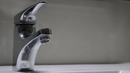 A man closing the dripping faucet to save water. The faucet was dripping for a long time. This shoot is a close up in the faucet. We are in the bathroom.