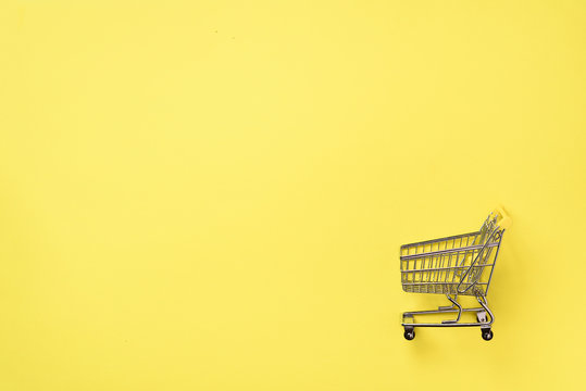 Shopping cart on yellow background. Minimalism style. Creative design. Top view with copy space. Shop trolley at supermarket. Sale, discount, shopaholism concept. Consumer society trend