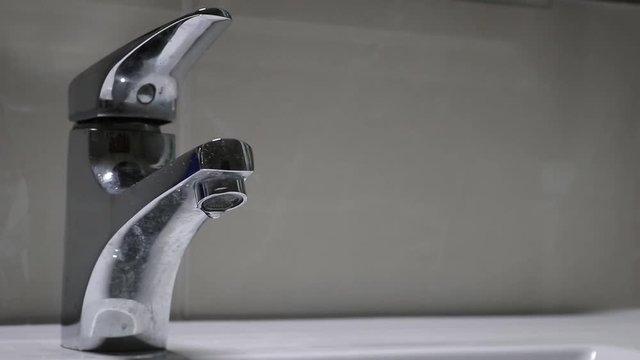 A man closing the dripping faucet to save water. The faucet was dripping for a long time. This shoot is a close up in the faucet. We are in the bathroom.
