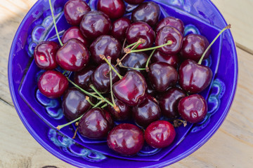 blue plate of ripe sweet cherry on  wooden table