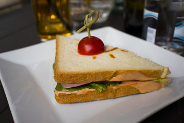 sandwich with cheese ham green tomato in a white plate on the table in the cafe on the background of drinks and food