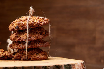 Bunch of chocolate biscuits on a round wood log over rustic wooden background, close-up, selective focus.