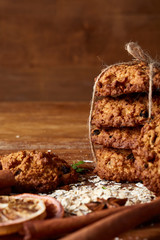 Christmas composition with chocolate biscuits, cinnamon and dried oranges on wooden background, close-up.